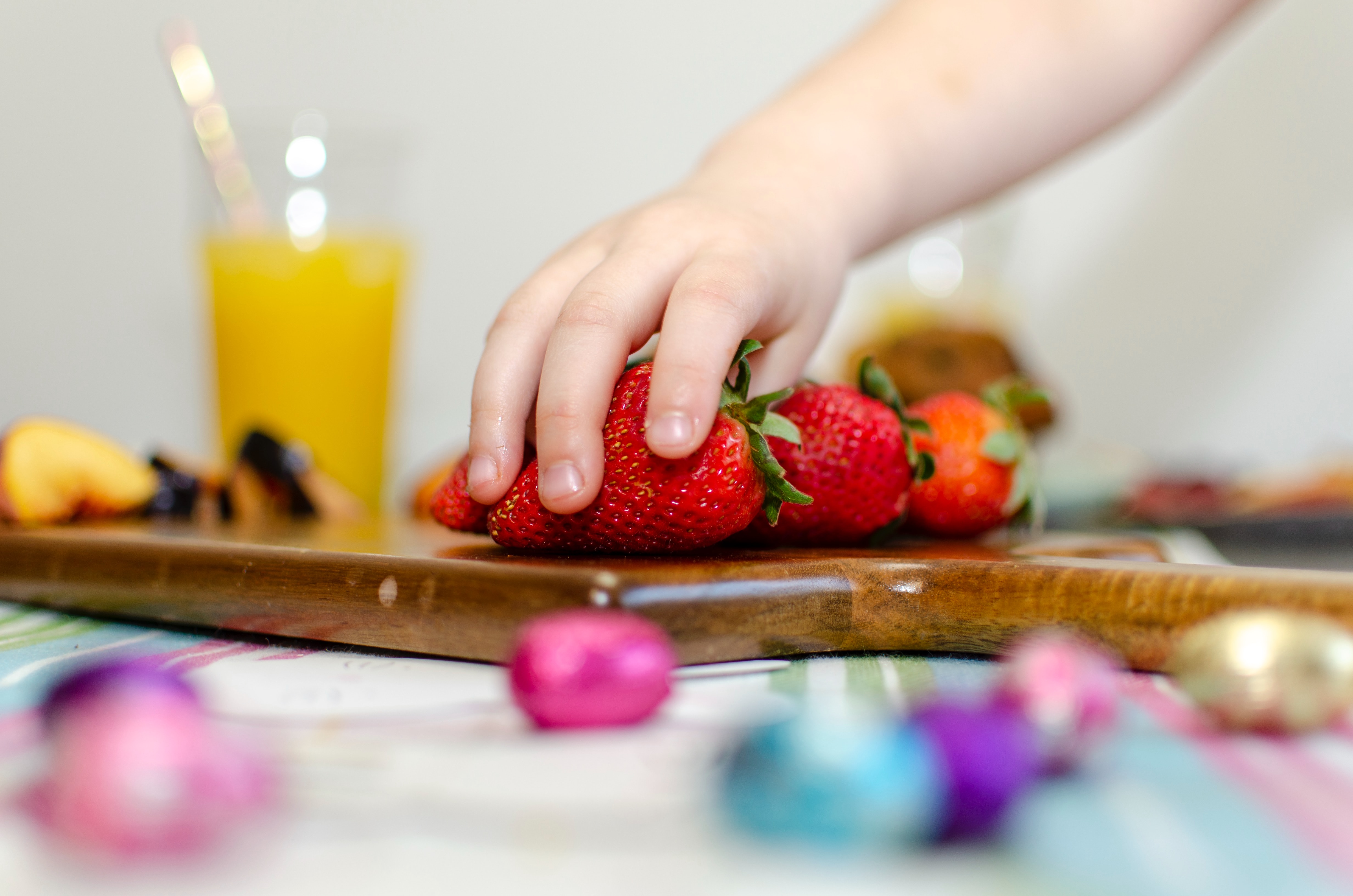 small hand reaching for strawberries on wooden chopping board